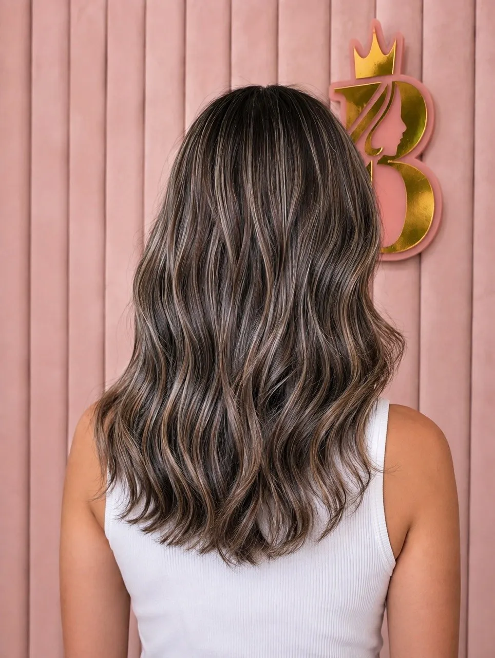 Soft balayage waves against the salon's blush-pink panelled wall and gold Beautylicious emblem