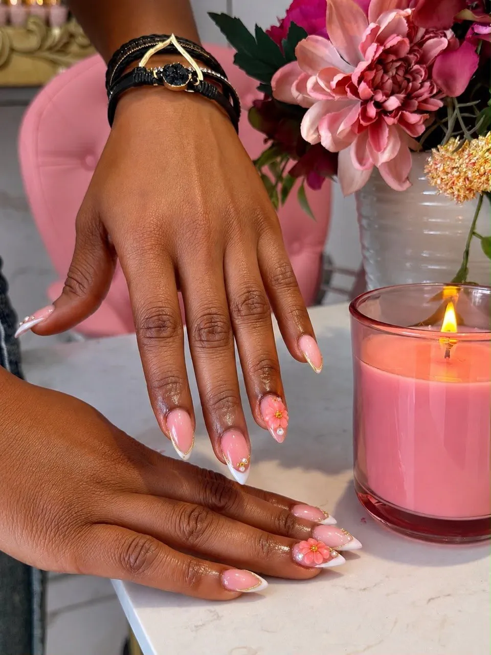 Gold-edged french tips with 3D flowers, posed by a pink candle